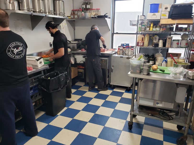 Chefs prepare food in a busy commercial kitchen with blue and white checkered floors.