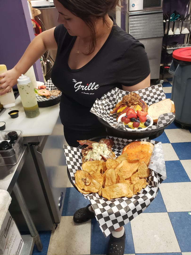 A server from The Grille at Franklin Court holds two baskets of food, including burgers, chips, and fruit.