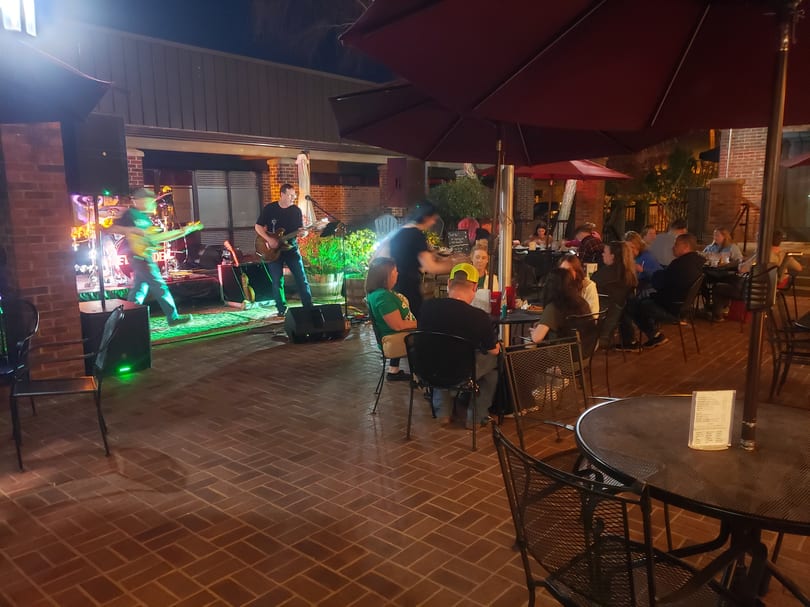 Outdoor patio at night with a live band performing for seated guests under umbrellas.